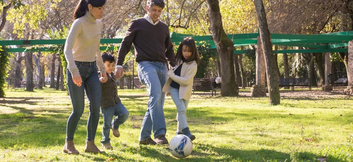 A family plays soccer together in a sunny park, enjoying quality time outdoors.